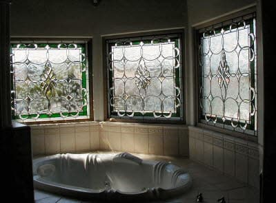 Bathroom corner with three beveled clear-glass windows framed in green over a built-in oval tub.